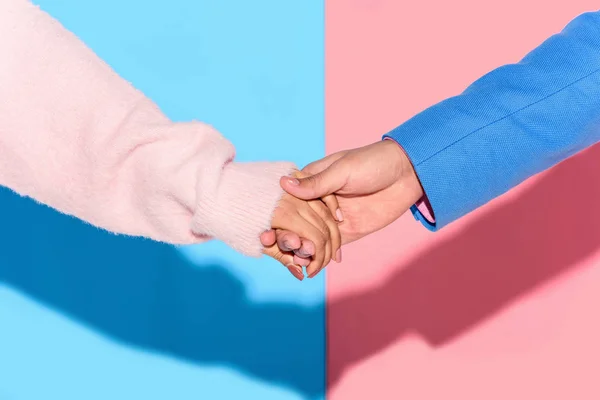 Vista de cerca de la pareja cogida de la mano sobre fondo rosa y azul - foto de stock