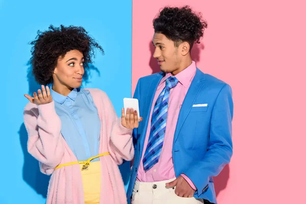 Молодой африканский американец удивленный девушка показывает мужчина экран телефона на розовом и синем фоне — стоковое фото