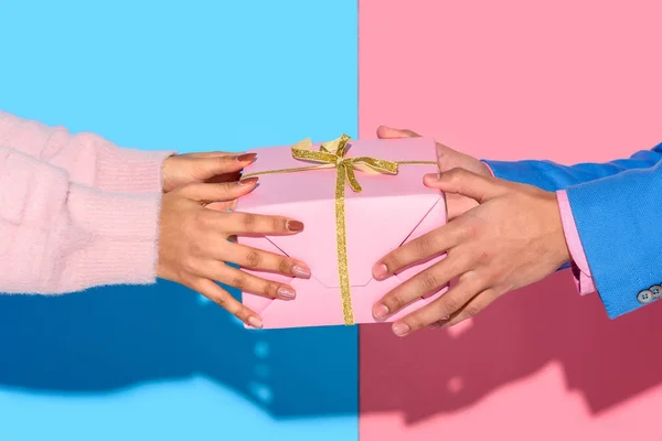 Close-up view of man giving girl gift box on pink and blue background — Stock Photo