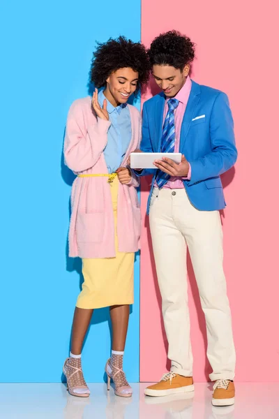 Pareja sonriente usando tableta digital sobre fondo rosa y azul - foto de stock