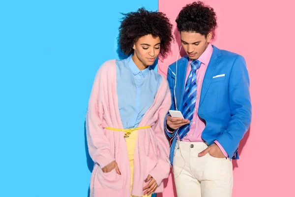 Hermosa pareja escuchando música en el teléfono inteligente sobre fondo rosa y azul - foto de stock