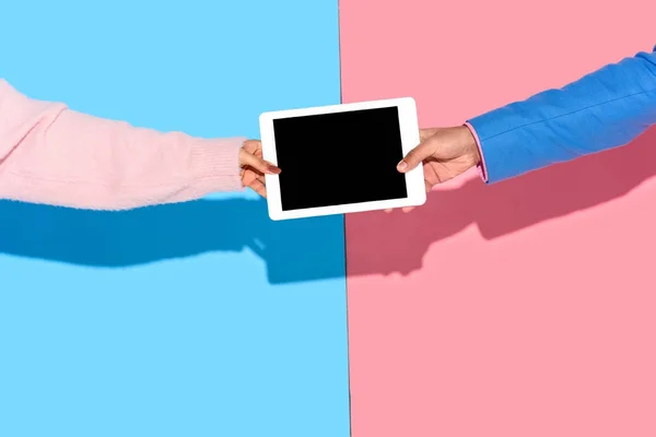 Image recadrée des mains tenant la tablette numérique sur fond rose et bleu — Photo de stock