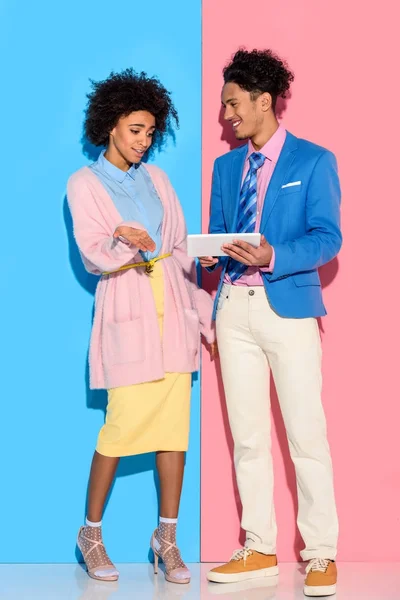Счастливая пара с помощью цифровой таблички на розовом и голубом фоне — стоковое фото