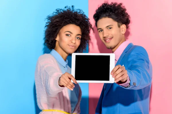 Smiling couple holding digital tablet in hands on pink and blue background — Stock Photo