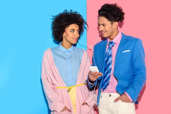 Jeune couple écoutant de la musique sur smartphone sur fond rose et bleu — Photo de stock