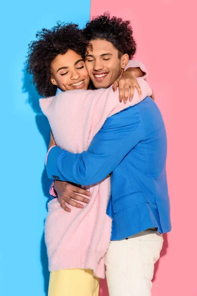 Encantadora pareja joven abrazándose unos a otros sobre fondo rosa y azul - foto de stock