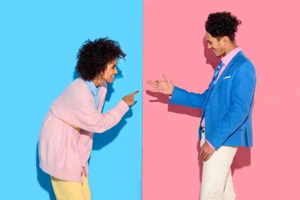 Feliz pareja haciendo gestos y haciendo graciosas sombras sobre fondo rosa y azul - foto de stock