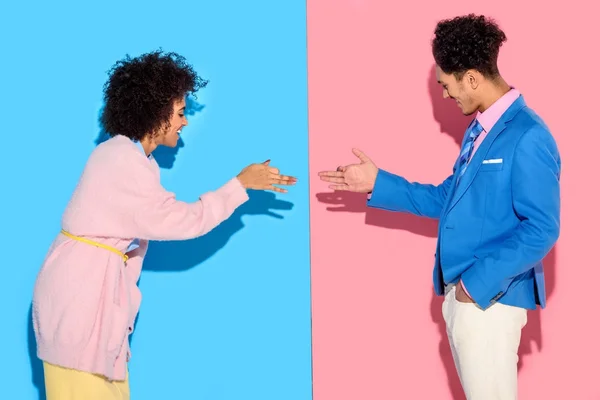 Sorrindo casal gesticulando e fazendo sombras engraçadas no fundo rosa e azul — Fotografia de Stock