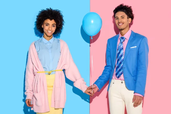 Young couple holding hands with air balloon on pink and blue background — Stock Photo