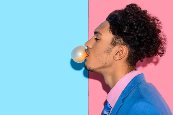 Primer plano del hombre guapo soplando goma de mascar sobre fondo rosa y azul - foto de stock