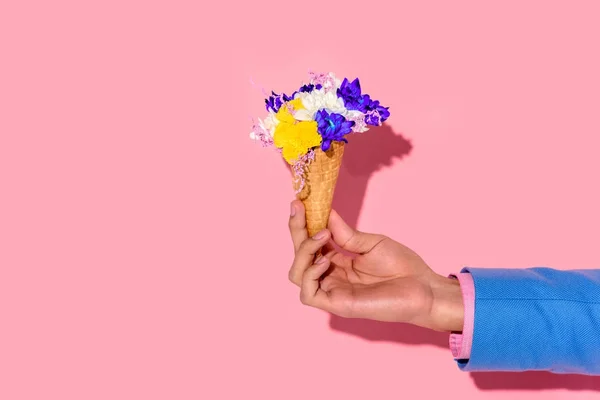 Cropped shot of african american man holding flowers in ice cream cone on pink wall background — Stock Photo