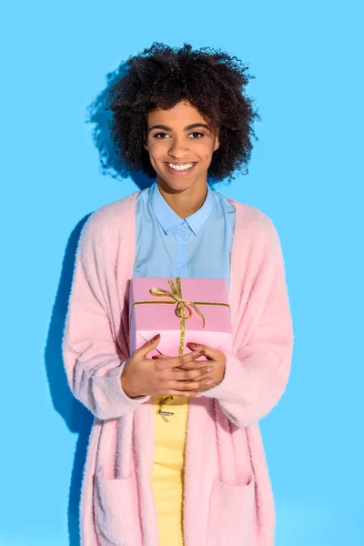 Portrait de femme afro-américaine joyeuse avec un cadeau dans les mains contre le mur bleu — Stock Photo