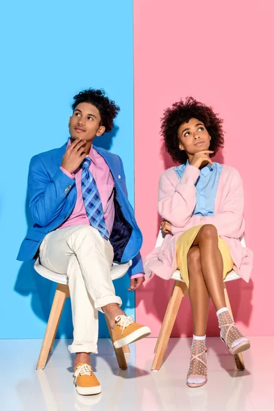 African american pensive couple sitting on chairs against pink and blue wall backdrop — Stock Photo