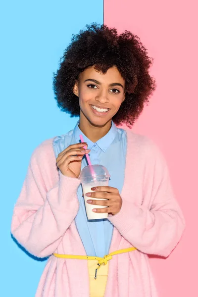Retrato de mujer afroamericana sonriente con vaso de leche sobre fondo de pared rosa y azul - foto de stock