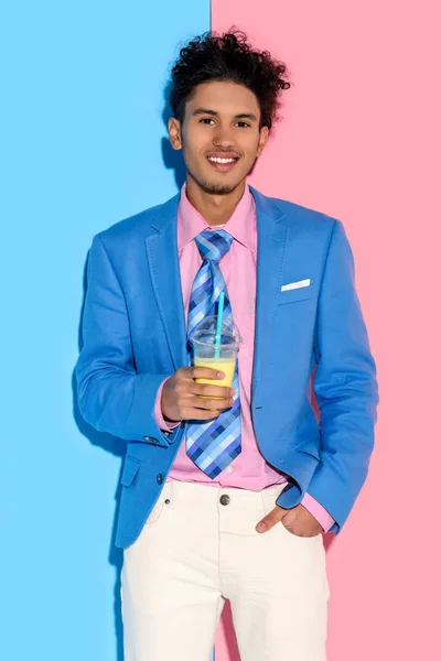 Retrato de homem americano africano sorridente com vidro de suco contra parede rosa e azul — Fotografia de Stock