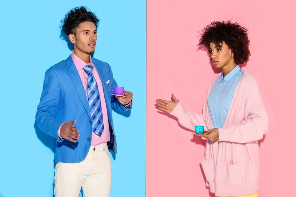 Elegante casal afro-americano com chávenas de brinquedo com fundo de parede rosa e azul — Fotografia de Stock