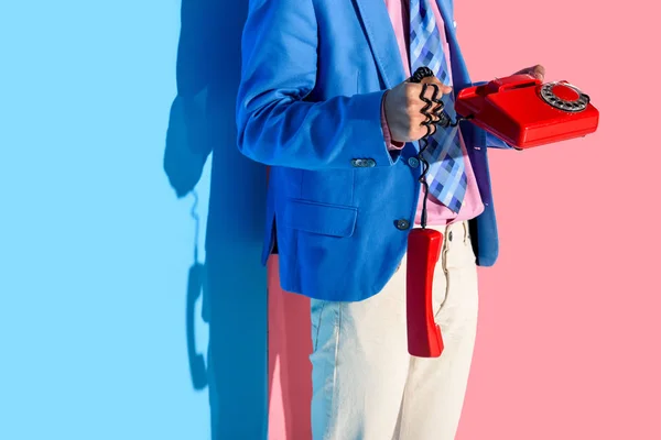 Midsection de hombre en traje formal con teléfono retro en las manos sobre fondo rosa y azul - foto de stock