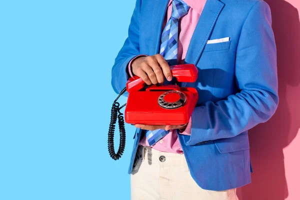 Midsection of man in formal suit with retro phone in hands  on pink and blue background — Stock Photo