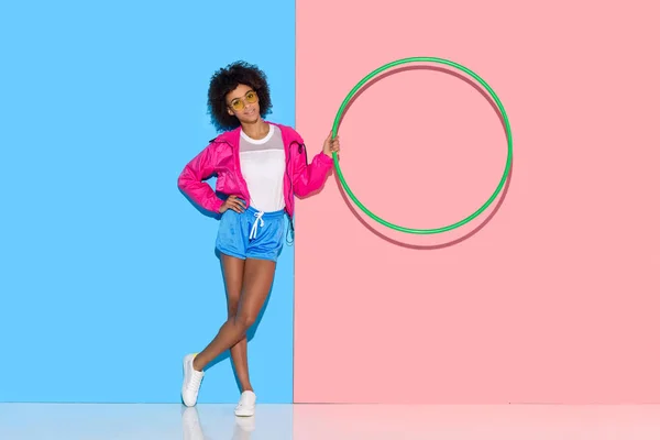 Woman in sportswear standing with hoop in hand on pink and blue background — Stock Photo