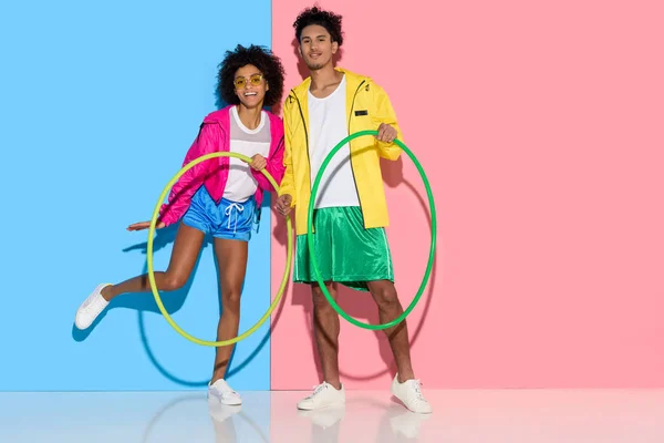 Deportiva pareja de pie con aros y mirando a la cámara en rosa y azul de fondo - foto de stock