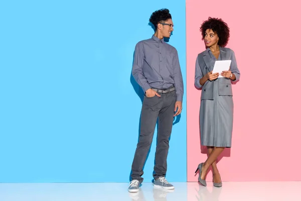 Jeune homme d'affaires afro-américain debout par fille avec une tablette dans les mains sur fond rose et bleu — Photo de stock