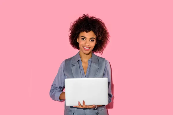 Молодой африканский американец улыбается бизнесвумен держа ноутбук на розовом фоне — стоковое фото
