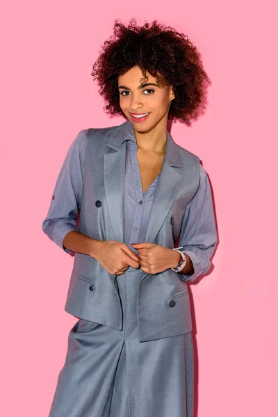 Joven amerciana africana sonriente en traje gris sobre fondo rosa - foto de stock