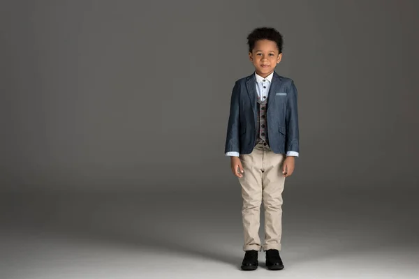 Чарівний афроамериканський хлопчик стоїть в костюмі на сірому — стокове фото