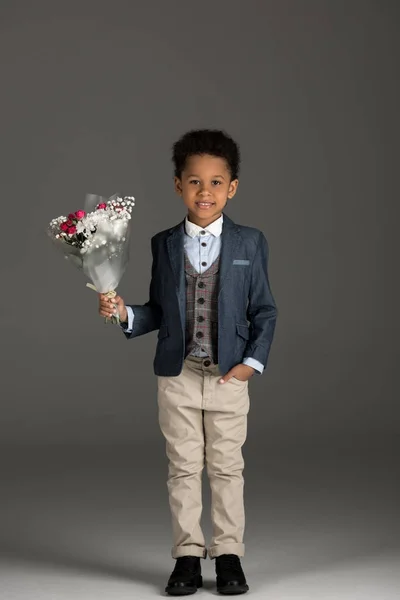 Bambino afroamericano sorridente in piedi con mazzo di fiori su grigio — Foto stock