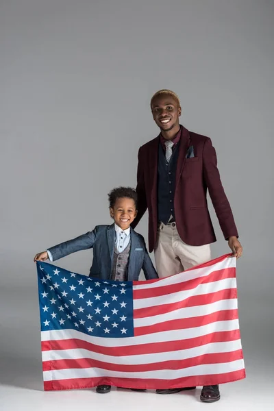 Афро-американської родини, дивлячись на камеру при хлопчик тримає американський прапор в руки на сірий фон — стокове фото