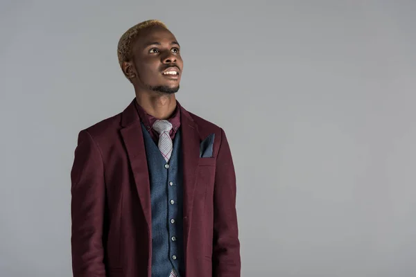 Lächelnder Afroamerikaner in Jacke, der isoliert auf grau nach oben schaut — Stockfoto