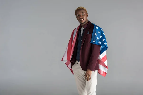 Афроамериканський чоловік з американським прапором на плечах дивиться на камеру ізольовано на сірому — стокове фото