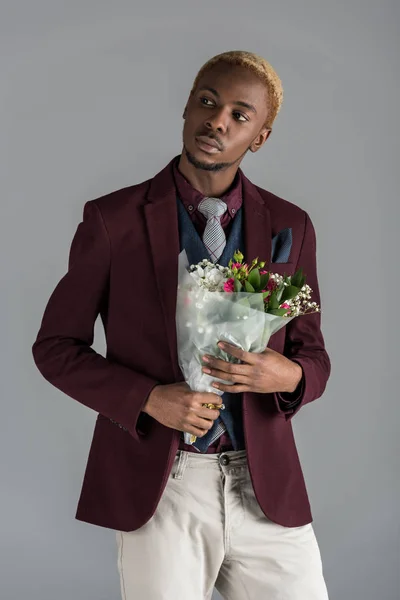 Hombre afroamericano pensativo con flores en las manos mirando hacia otro lado aislado en gris - foto de stock