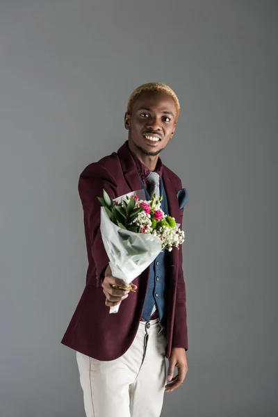 Smiling african american man with bouquet in hand isolated on grey — Stock Photo