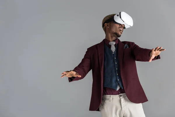 Young african american in vr headset  with arms outstretched on grey background — Stock Photo