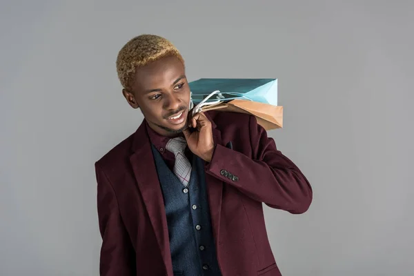 Smiling man with paper shopping bags in hand over shoulder on grey background — Stock Photo