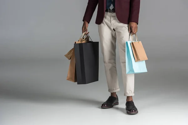 Seção baixa de homem com sacos de compras de papel em fundo cinza — Fotografia de Stock
