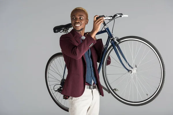 Sorridente afro-americano homem segurando bicicleta em mãos isoladas em cinza — Fotografia de Stock