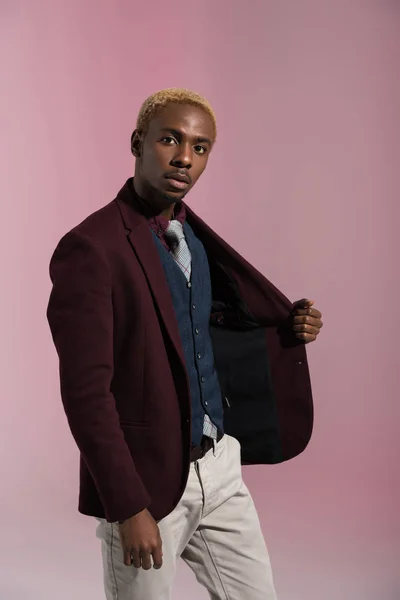 Afrikanisch-amerikanischer Mann blickt in die Kamera, während er die Seite seiner Jacke auf rosa Hintergrund hält — Stockfoto