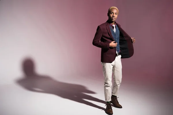 Young african man in red jacket standing on pink background — Stock Photo