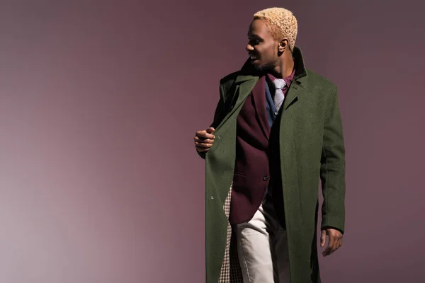 Stylische junge afrikanisch-amerikanische Mann trägt grünen Wintermantel isoliert auf violettem Hintergrund — Stockfoto