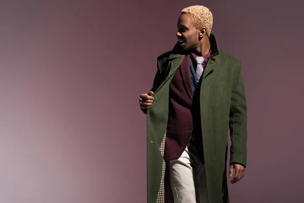 Jeune homme afro-américain élégant portant un manteau d'hiver vert isolé sur fond violet — Photo de stock