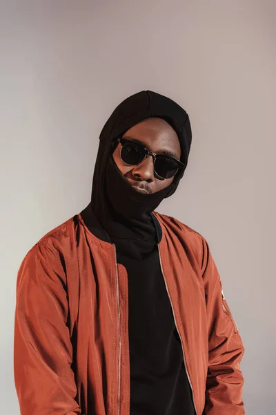 Stylish young african american man wearing hood with face mask isolated on light background — Stock Photo