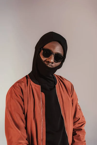 Elegante joven afroamericano con capucha con mascarilla aislada sobre fondo claro - foto de stock