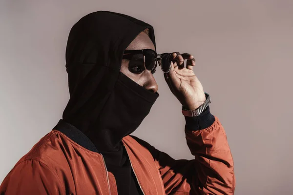 Elegante joven afroamericano con capucha con mascarilla aislada sobre fondo claro - foto de stock