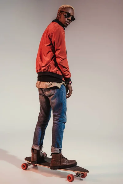 Stylish young african american skater standing on longboard — Stock Photo