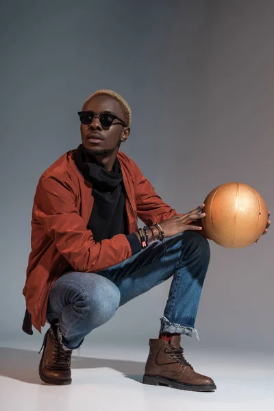 Elegante jovem afro-americano sentado com bola de basquete nas mãos — Fotografia de Stock