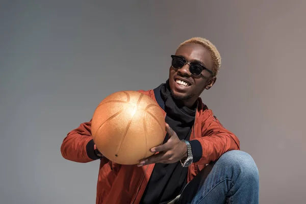 Стильний молодий афроамериканський усміхнений чоловік тримає баскетбольний м'яч ізольований на світлому фоні — стокове фото