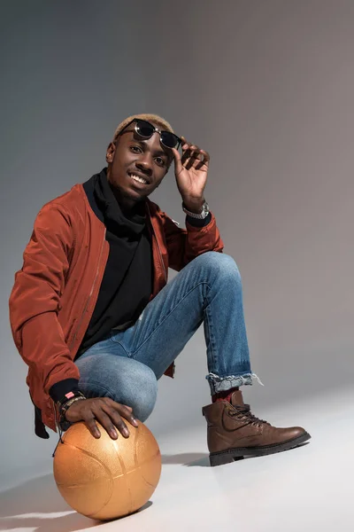 Elegante joven afroamericano sonriente hombre sosteniendo pelota de baloncesto en el suelo - foto de stock