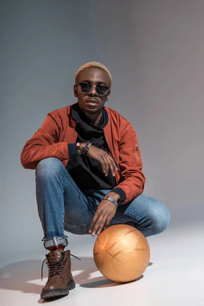 Stylish young african american man sitting with basketball ball on floor — Stock Photo